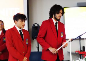 Two students in red blazers light candles.