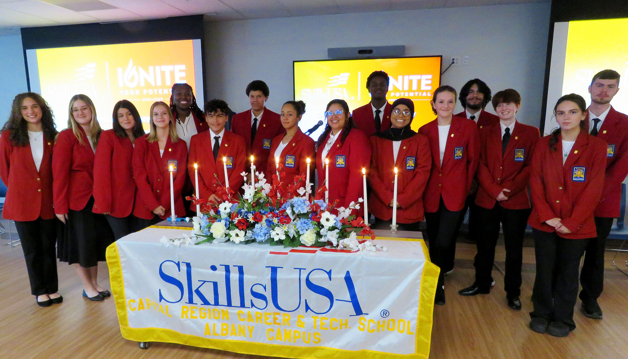 Teenagers in red blazers stand behind a table with candles and a table cloth that says SkillsUSA.